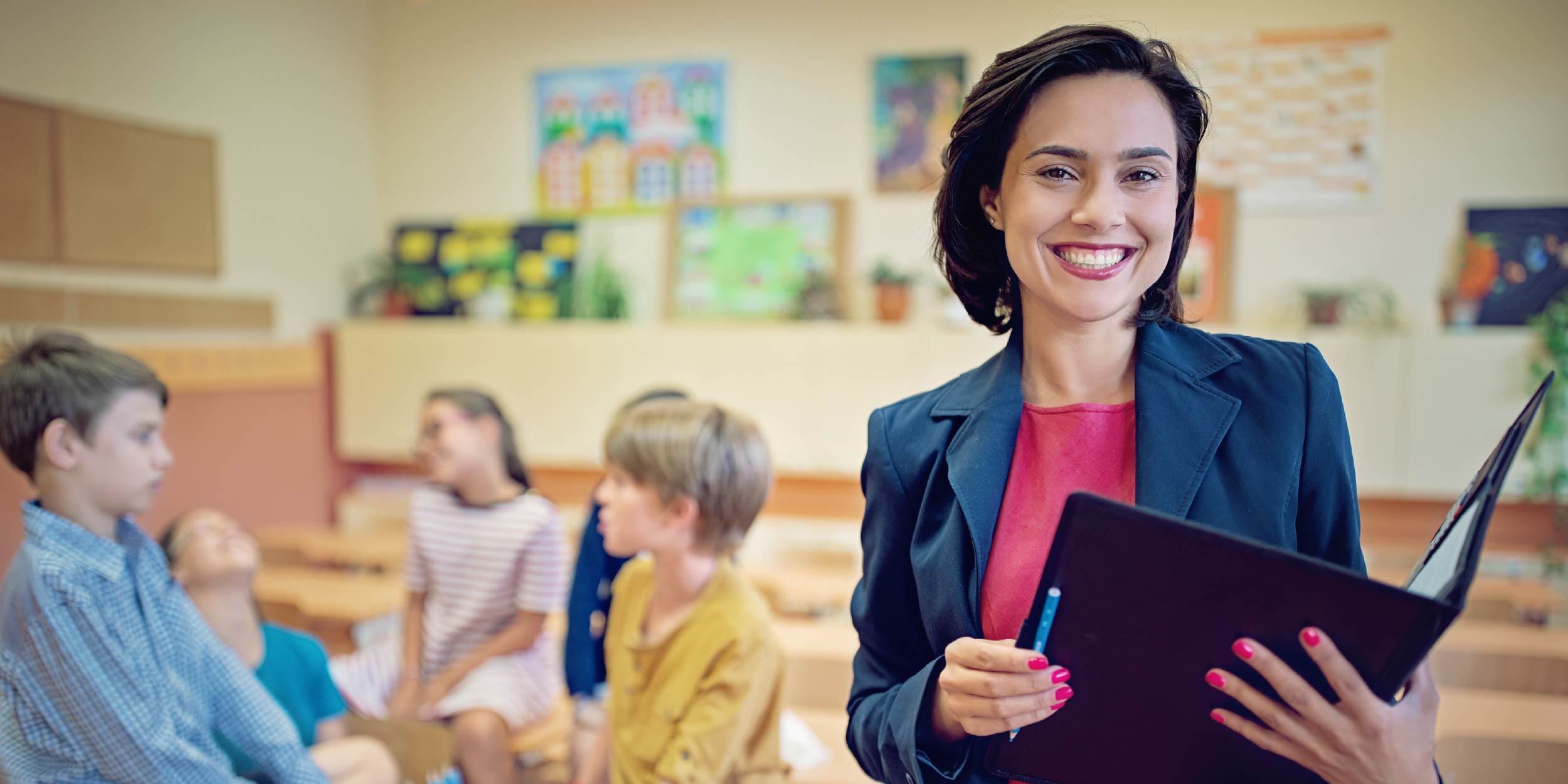 A superintendent standing in the foreground holding a binder with a group of children in the background