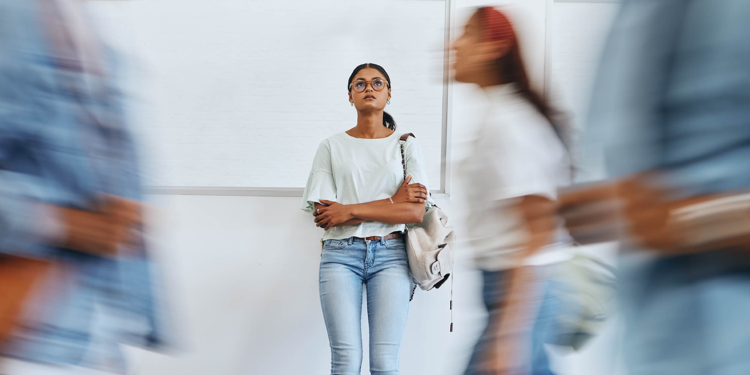 A person standing alone in a hallway with people going by 