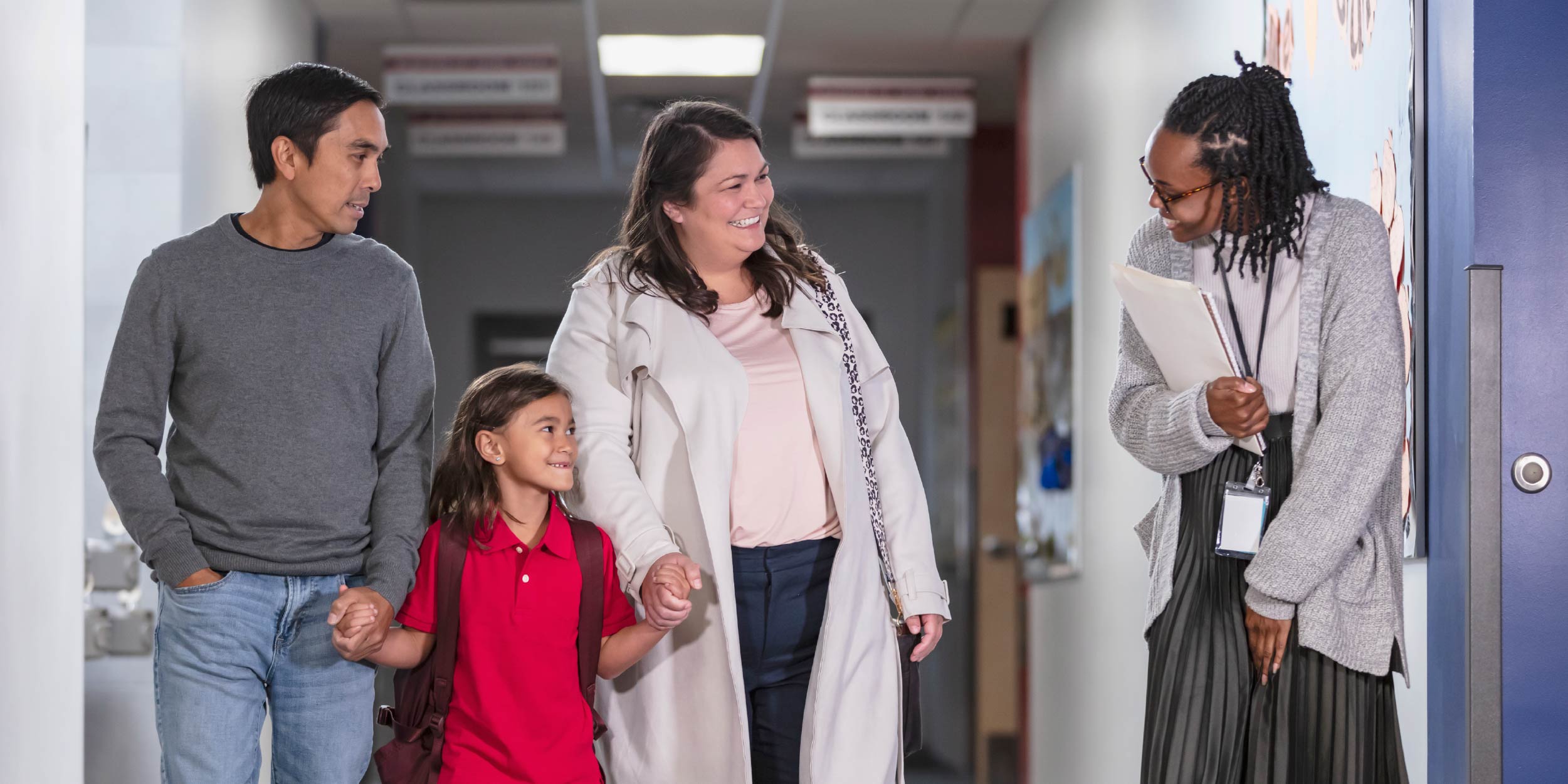 A teacher talking to a family and student in a school hallway