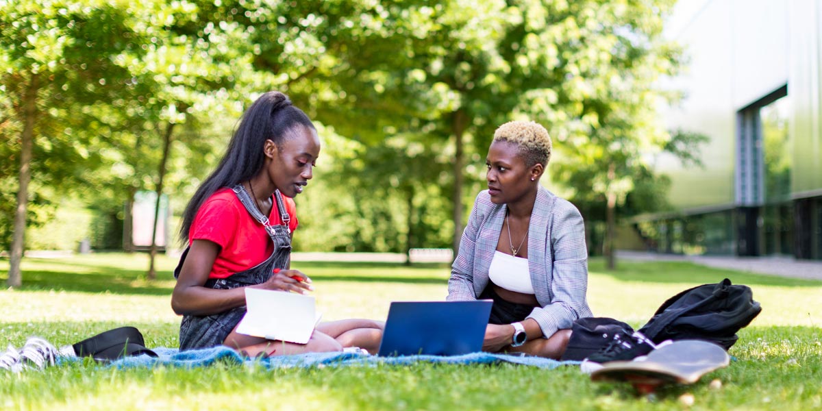 two students outside sitting in the grass