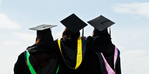 The backs of three people wearing graduation caps and gowns