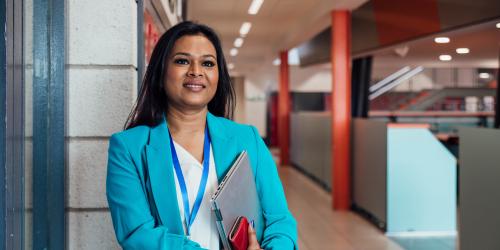 A person standing in a school with a laptop and a school badge