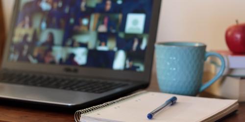A close up of a notebook with pen and a laptop open in the background with a video conference call