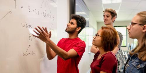 Students standing by a white board solving a math problem