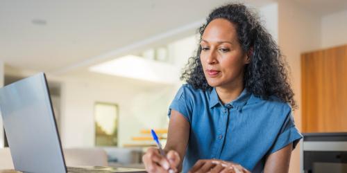 Person working on their computer while writing notes